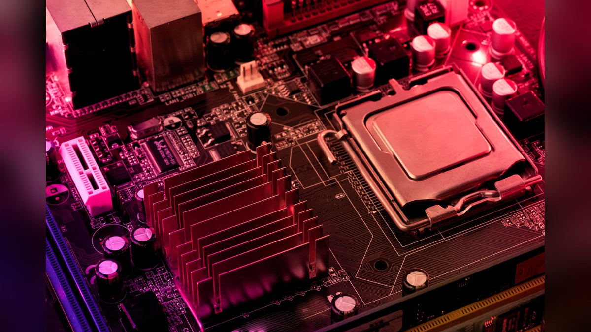 Close-up of a motherboard CPU socket with an installed processor and a finned heatsink under pink and purple light