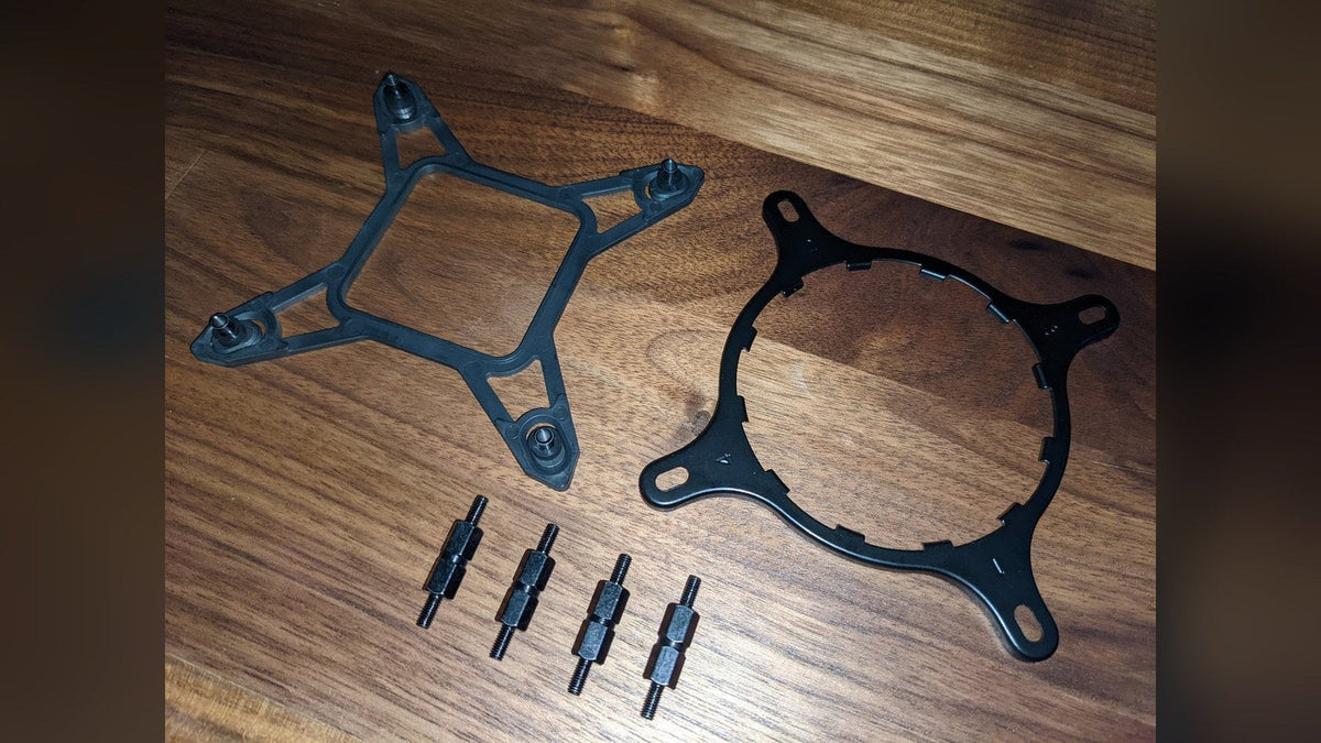 AIO cooler mounting hardware on a wood desk: a black backplate, round retention bracket and four standoffs