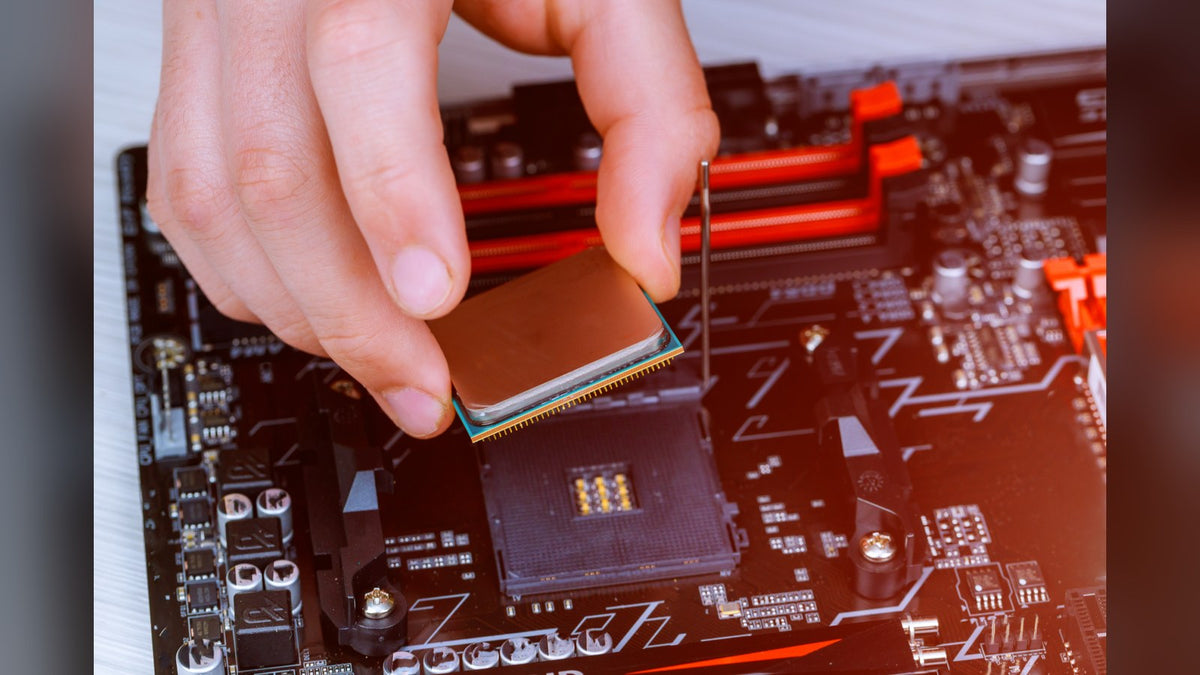 Hand lowering a processor into the CPU socket of a black and red motherboard